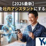 2026年最新、作業着を着た建設業の社長がスマートフォンを持ち、隣にいる先進的で親しみやすいAIアシスタントと協力して日報や現場書類を丸投げ作成し笑顔になっている様子。右下にはYM企画のグラデーションロゴバッジ。